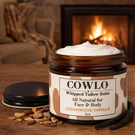 Cowlo Whipped Tallow Balm jar with a background of cedarwood and vanilla