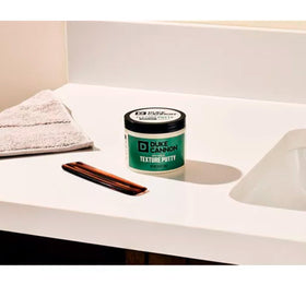 Duke Cannon Dry Hold Texture Putty on a bathroom shelf