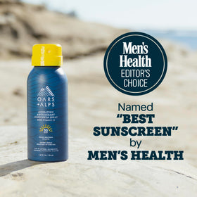 Oars + Alps SPF 50 Sunscreen Spray bottle side view on a beach