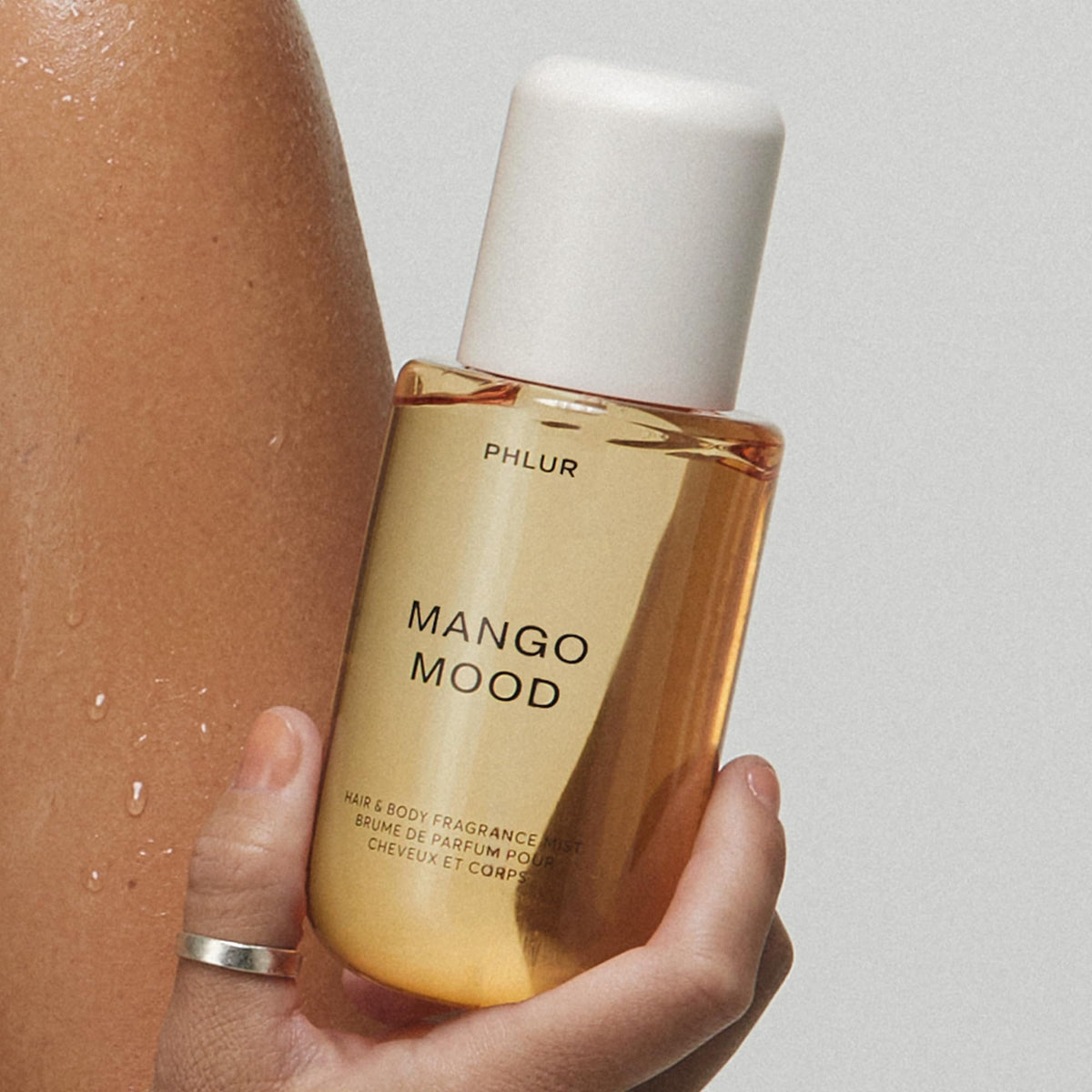 PHLUR Mango Mood Body Mist surrounded by tropical flowers