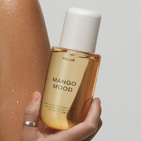PHLUR Mango Mood Body Mist surrounded by tropical flowers